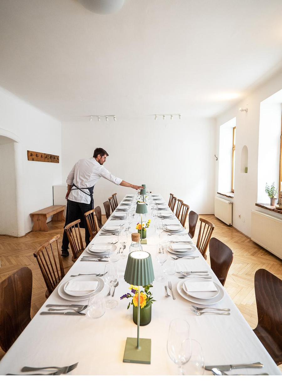 Koch deckt eine lange Tafel in einem hellen Saal ein