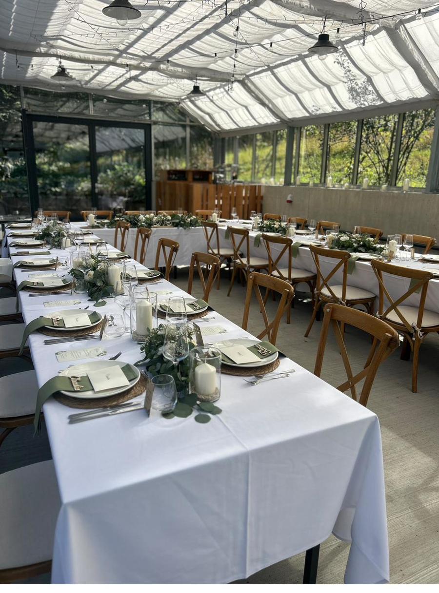 Hochzeitstafel im Glashaus mit weißem Leinen und Eukalyptus-Girlande